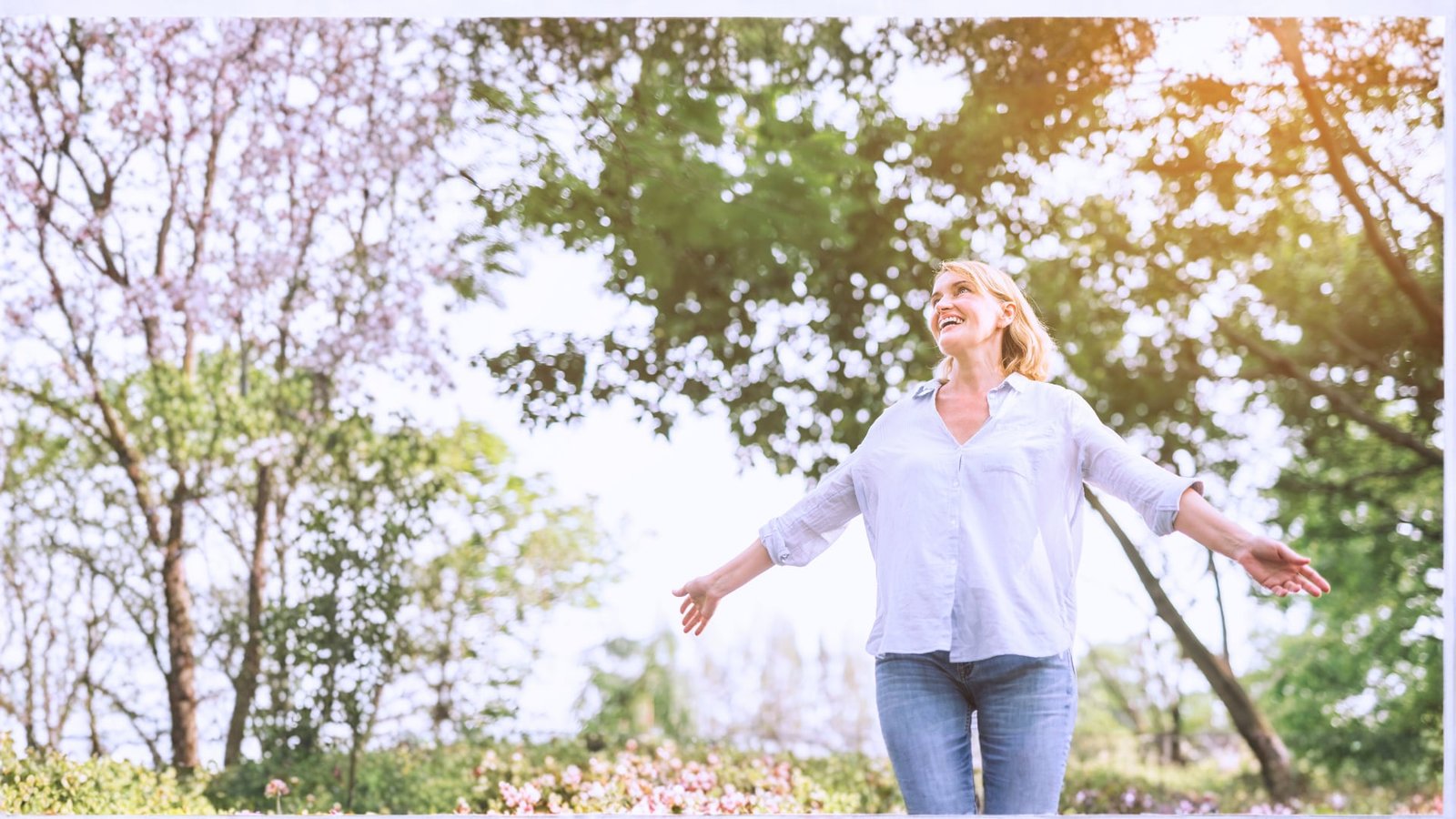 Una donna sorridente, con le braccia aperte, in un parco fiorito